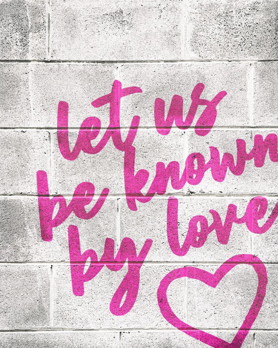 "Pink graffiti 'Let us be known by love' on a gray brick wall, featuring a heart symbol, emphasizes community and faith."
