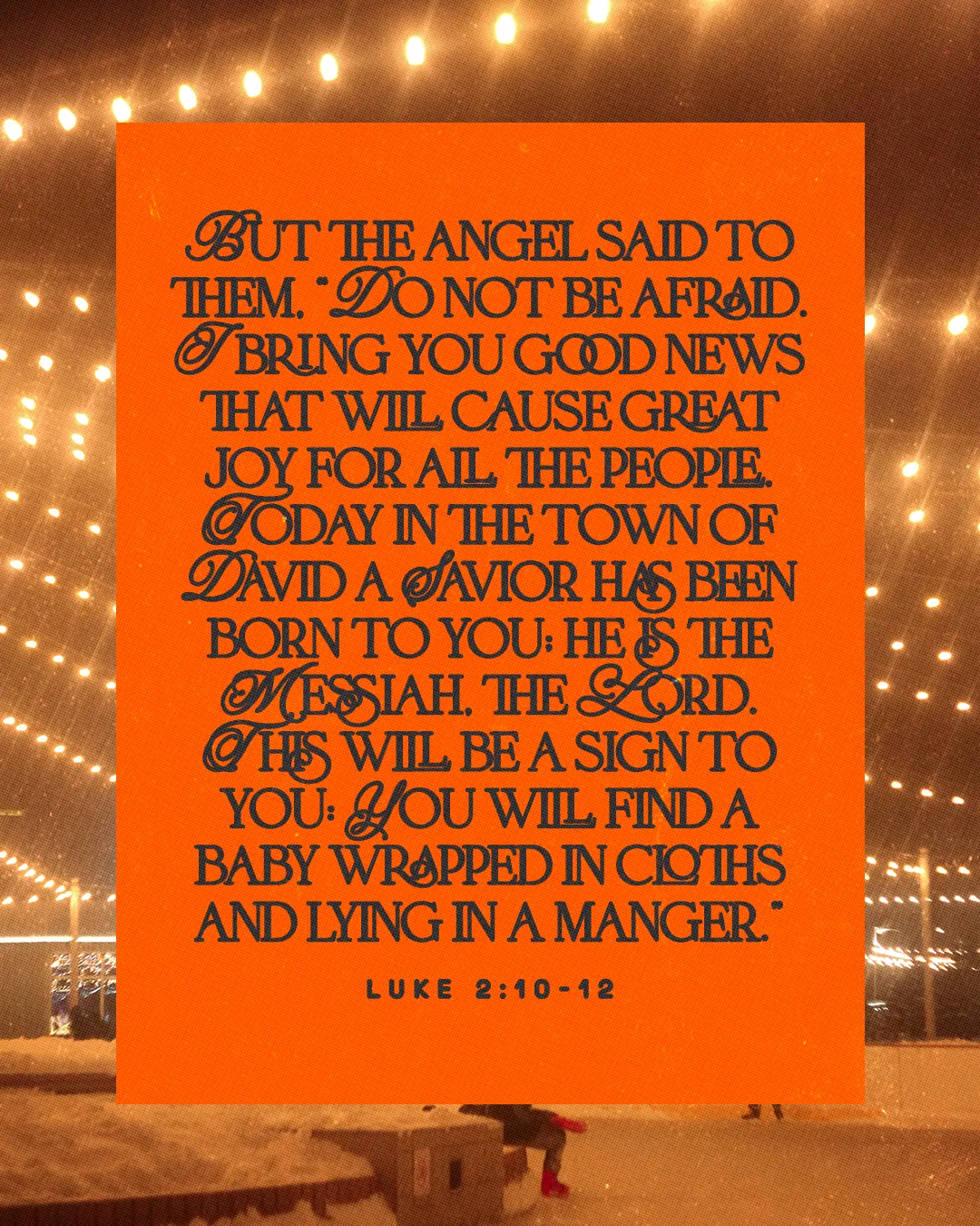 Luke 2:10-12 angel announcement text in dark brown on an orange block over warm string lights at night