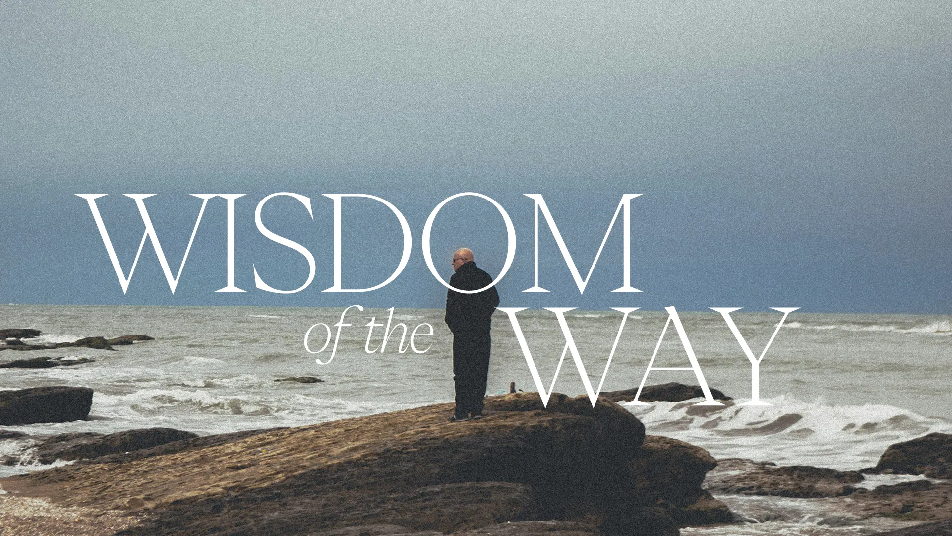 Person standing on rocky shore, gazing at the ocean, embodying contemplation and spiritual wisdom.